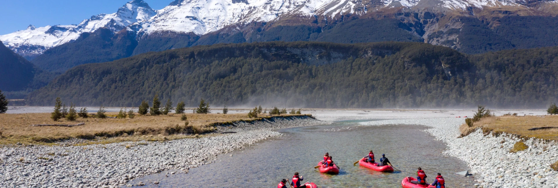 Group paddling Funyaks on the Dart River surrounded by mountains.