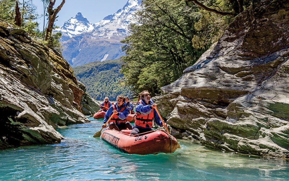 Couple exploring Dart River in Funyak inflatable canoes with snow-capped peaks and forest backdrop