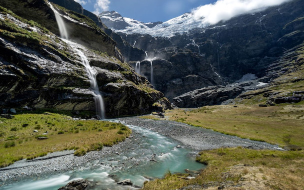 Valley with waterfalls, river and mountains with helicopter parked on grass