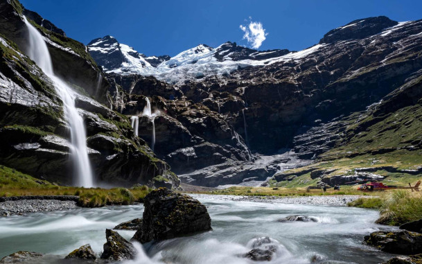 Valley with waterfalls, river and mountains with helicopter parked on grass