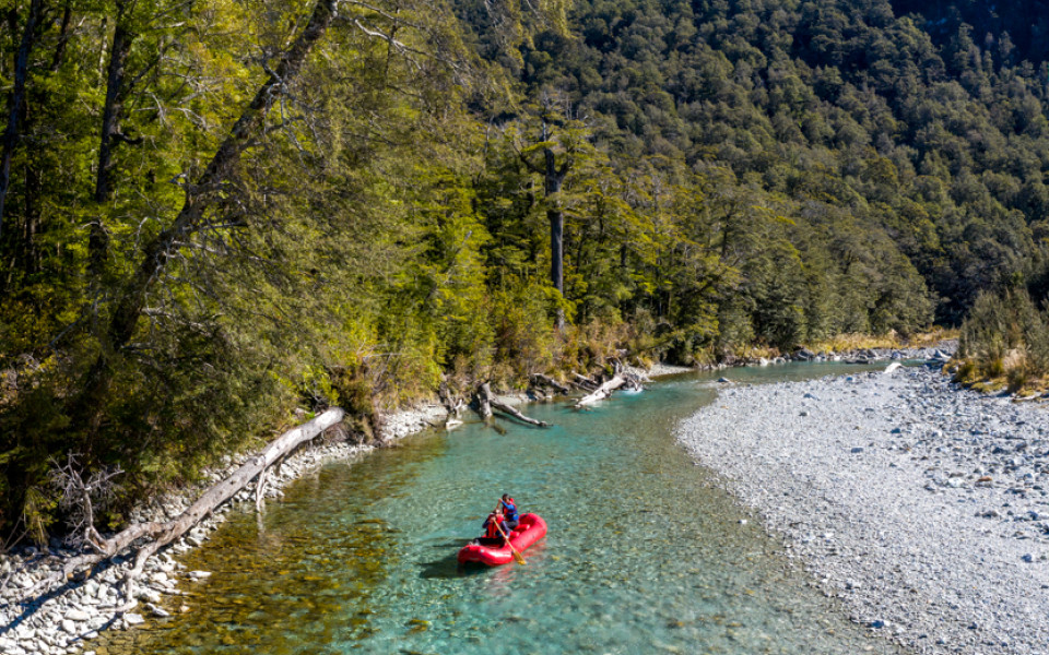 Funyak paddlers gliding past riverbank with native bush