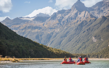 Funyak paddlers surrounded by mountains and native forest in Mount Aspiring National Park.