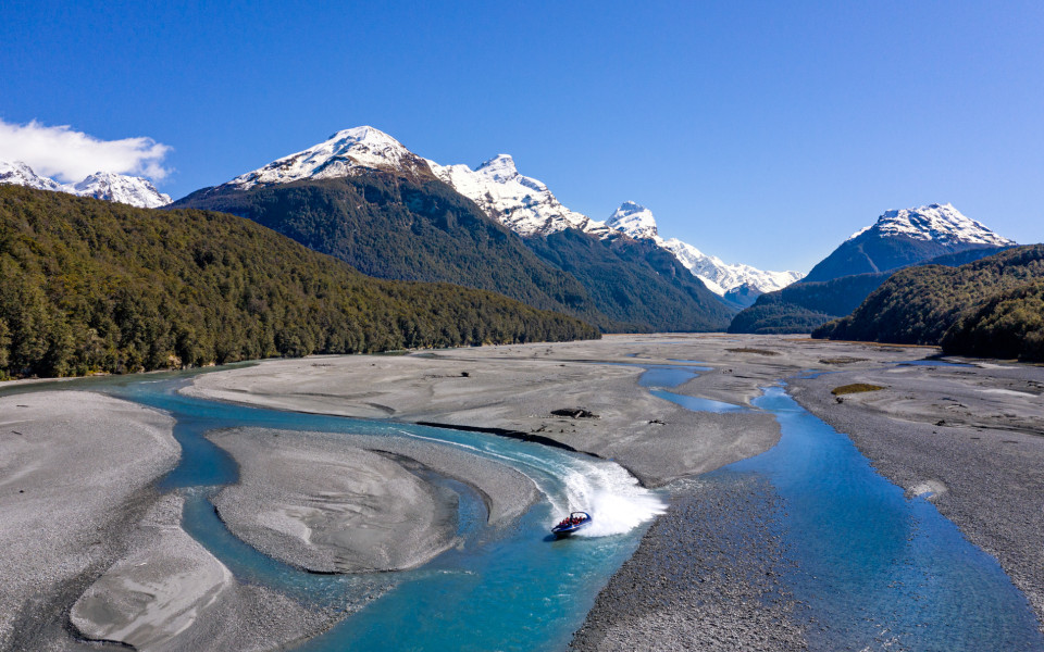 Jet boat speeding along the Dart River with snow-capped mountains in Mount Aspiring National Park
