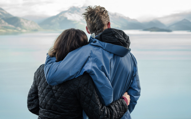 Couple standing with arms around each other, looking out at a scenic mountain view