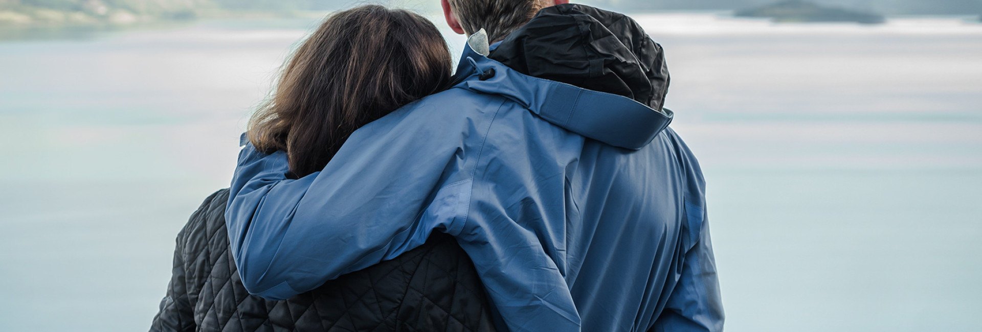 Couple standing with arms around each other, looking out at a scenic mountain view