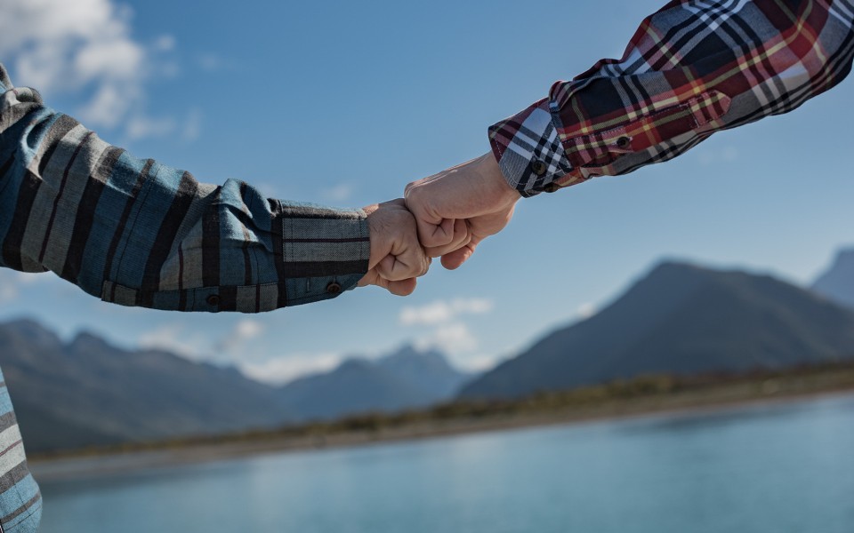 Two men joining knuckles with river and mountains in background