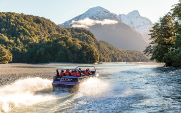 Visitors on board the Wilderness Jet boat on the Dart River, surrounded by native trees and towering mountains