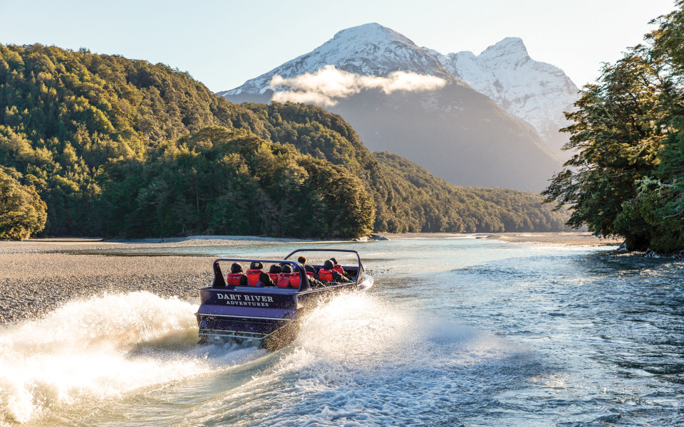 Visitors on board the Wilderness Jet boat on the Dart River, surrounded by native trees and towering mountains