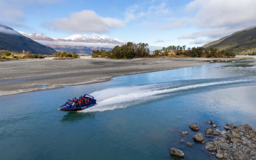 Jet boat speeding along the Dart River with water spraying behind