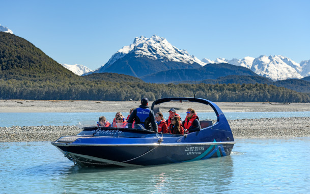 Guide talking to passengers on a Wilderness Jet boat on the Dart River with mountains in the background