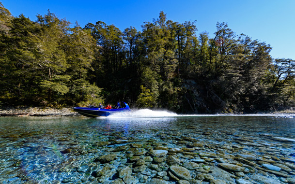 Jet boat speeding along the Dart River with water spray behind
