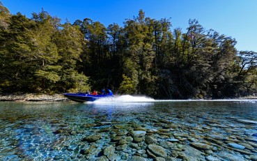 Jet boat speeding along the Dart River with water spray behind