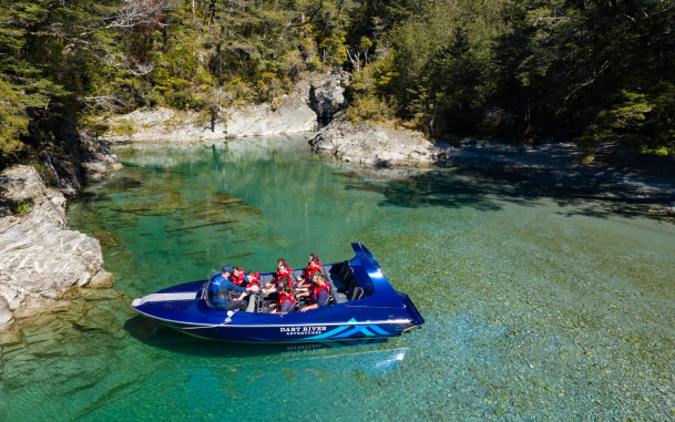 Guide talking to passengers on a Wilderness Jet boat on the Dart River with trees behind